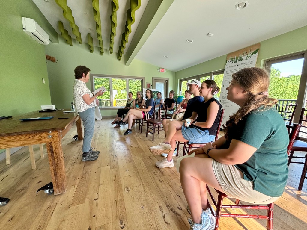 Sheila reading from her book while standing in front several people who are seated.